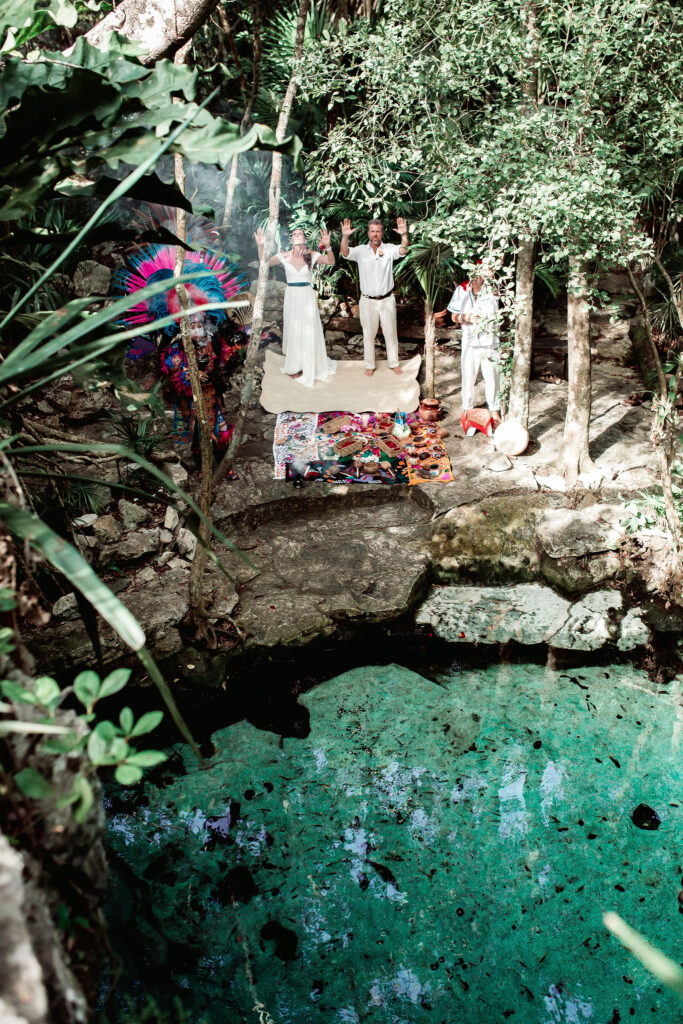 Pareja de pie en un cenote privado, rodeados de agua cristalina y formaciones naturales durante una boda consciente.