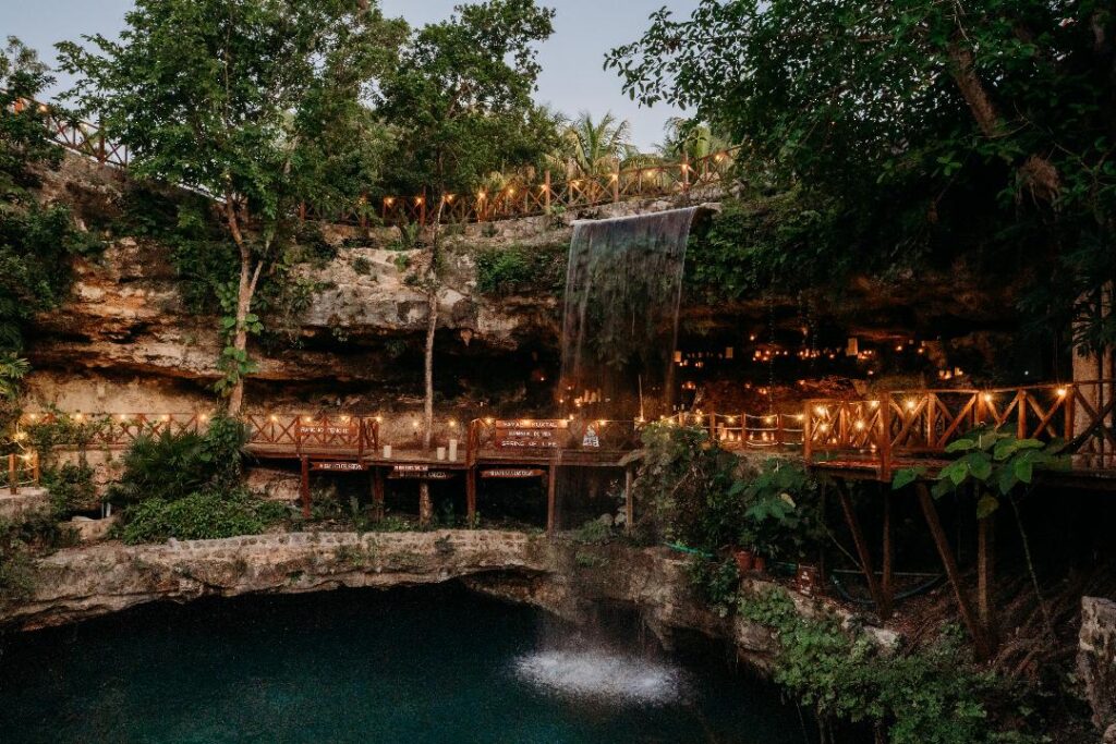 Couple and officiant performing a sacred wedding ritual inside a cenote with waterfall surroundings
