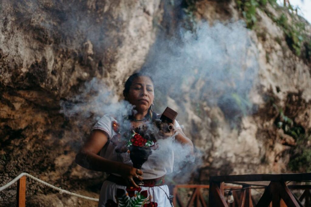 Mayan woman performing a smoke cleansing ritual on a jungle pathway leading to a cenote wedding ceremony