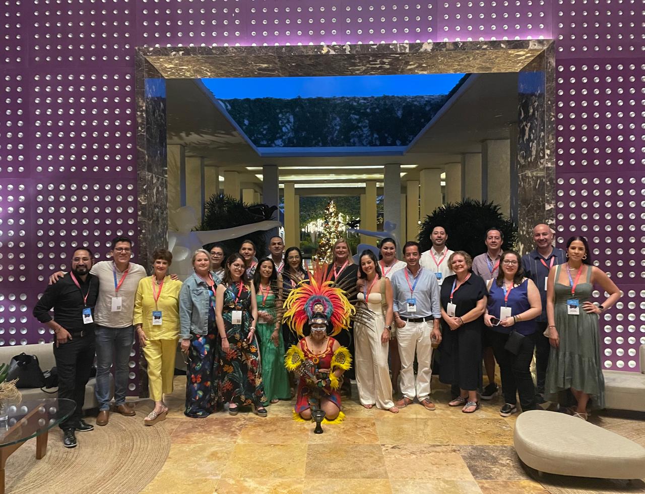 Grupo corporativo reunido alrededor de una danzante arrodillada en el lobby de un hotel tras la bienvenida