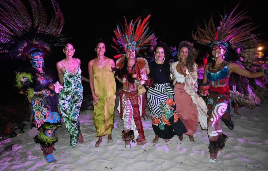 Invitados bailando en la playa de noche junto a danzantes con penachos de plumas