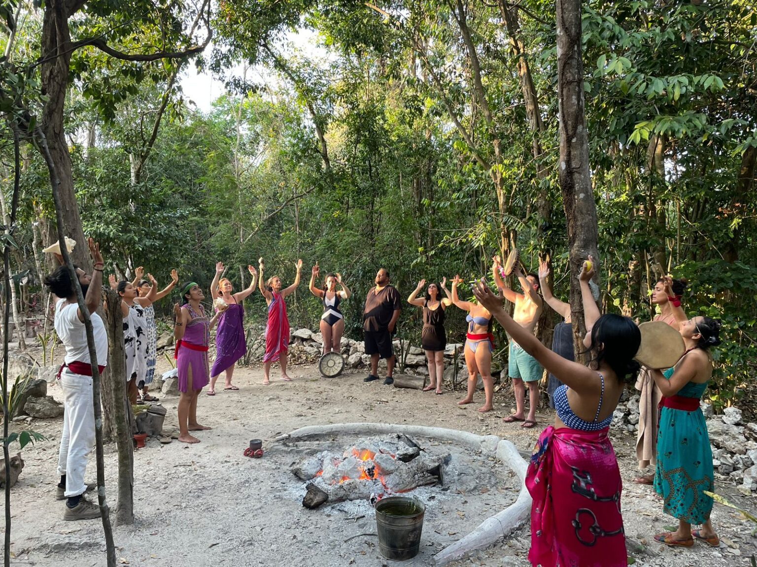 Circle of people with arms raised around a fire during a temazcal ceremony in the jungle