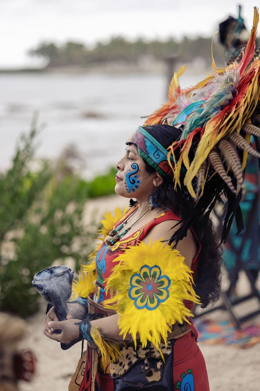 Danzante con penacho de plumas sosteniendo un sahumador humeante, con el mar detrás