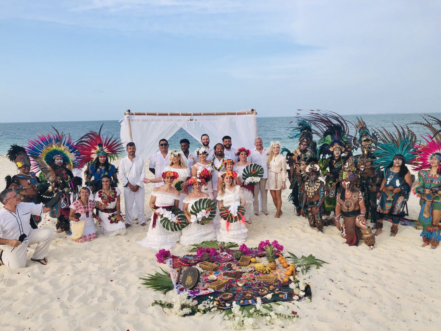 Una ceremonia de boda en la playa con todo el equipo maya prehispánico, los invitados y una ofrenda de flores sobre la arena