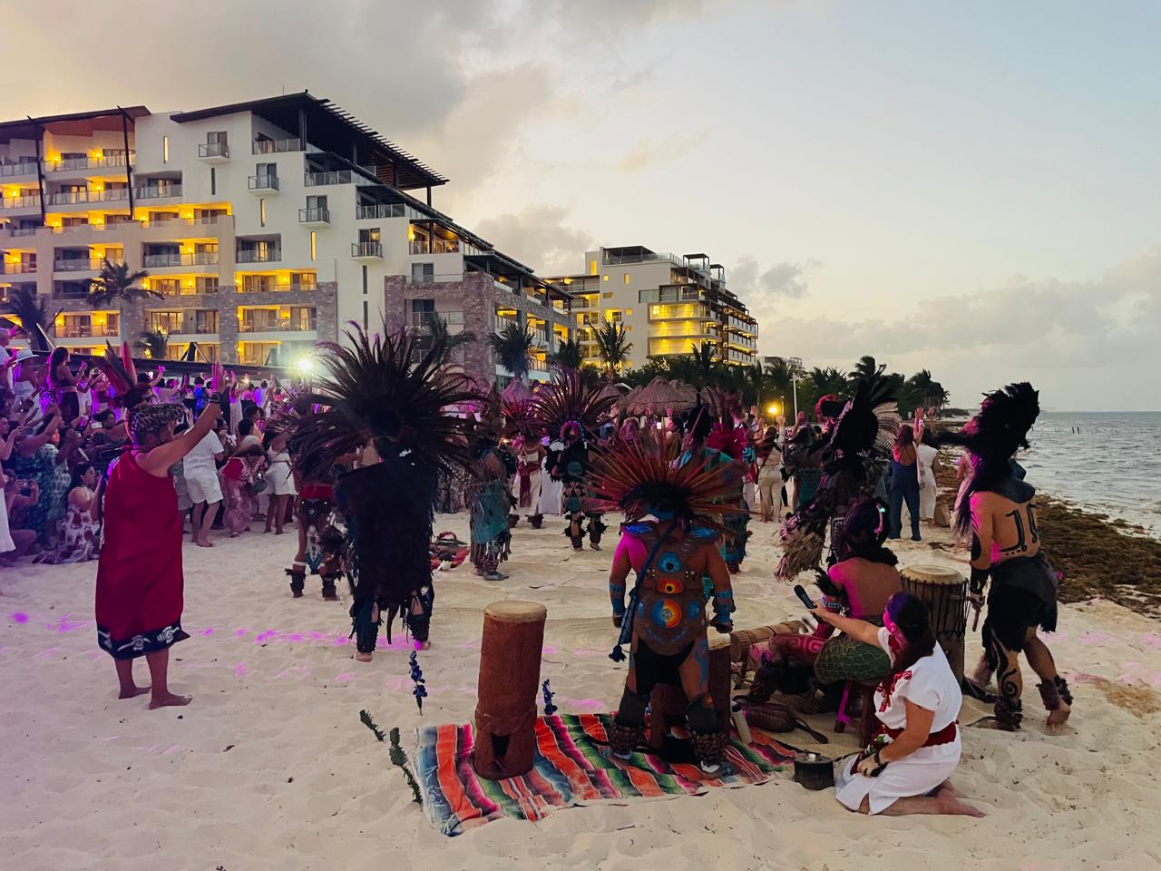 Danzantes y tambores en la playa al atardecer, con el grupo en círculo alrededor