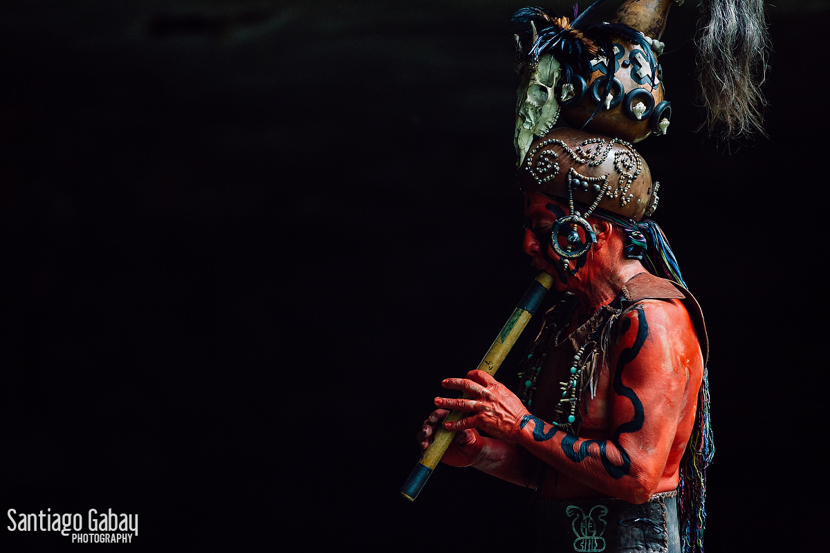 Un músico prehispánico con la cara pintada y penacho de plumas tocando una flauta