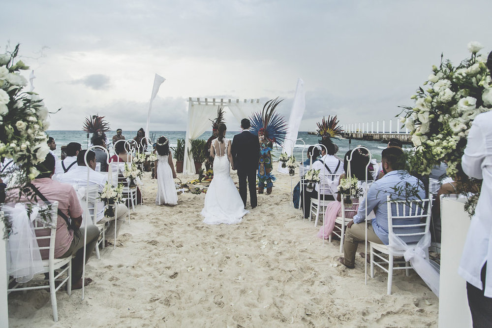Una novia camina por el pasillo en la playa entre los invitados, hacia el altar