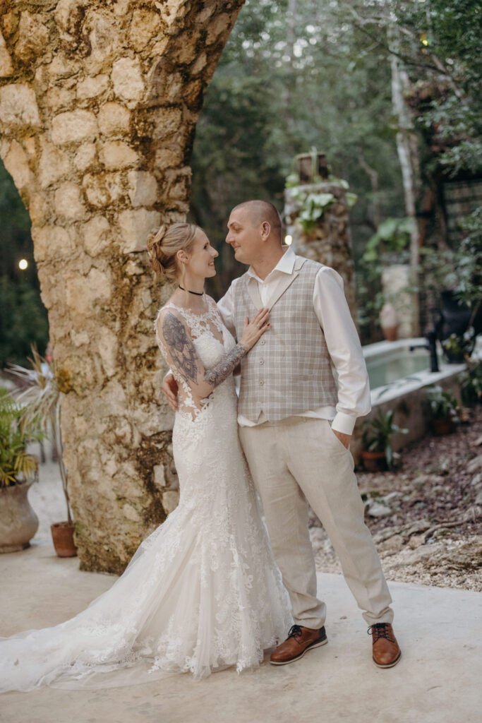 Bride and groom posing beneath tropical trees during spiritual wedding in Riviera Maya