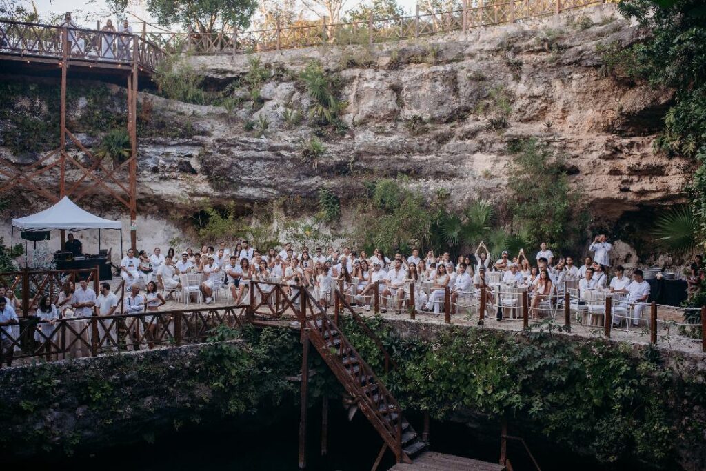 Wide view of a cenote wedding ceremony with guests gathered around a natural jungle venue in Mexico